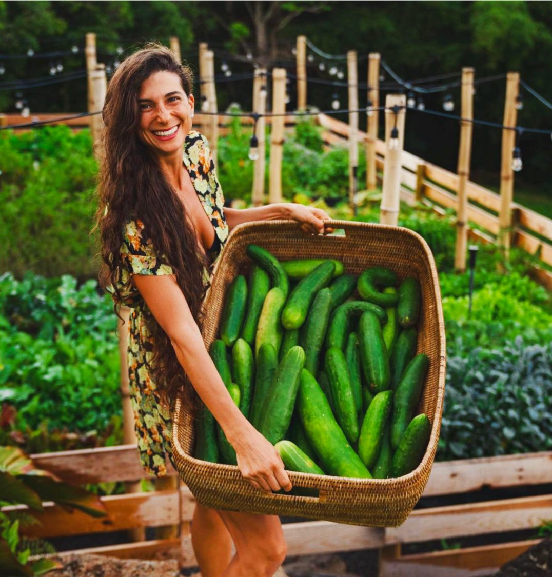 Kristina in her garden holding a big basket of cucumbers