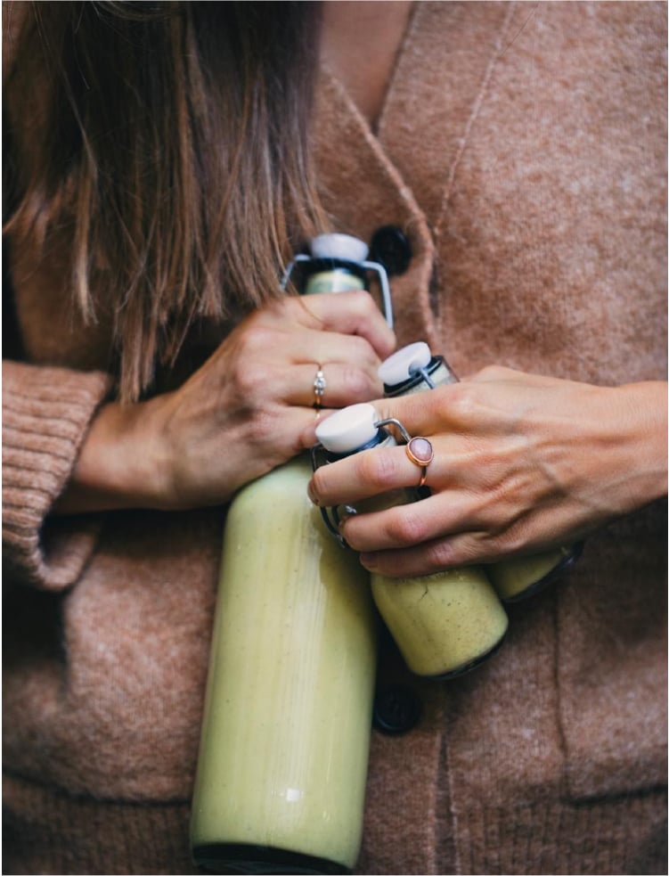 A woman in a brown sweater holding bottles of juice tightly.