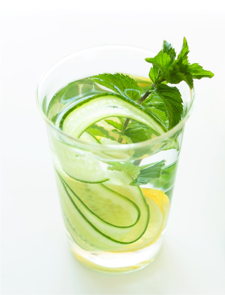 A glass of water with mint and a thin slice of cucumber