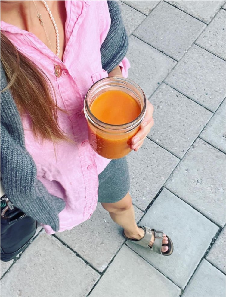 Woman in a pink blouse standing with a glass jar of orange juice