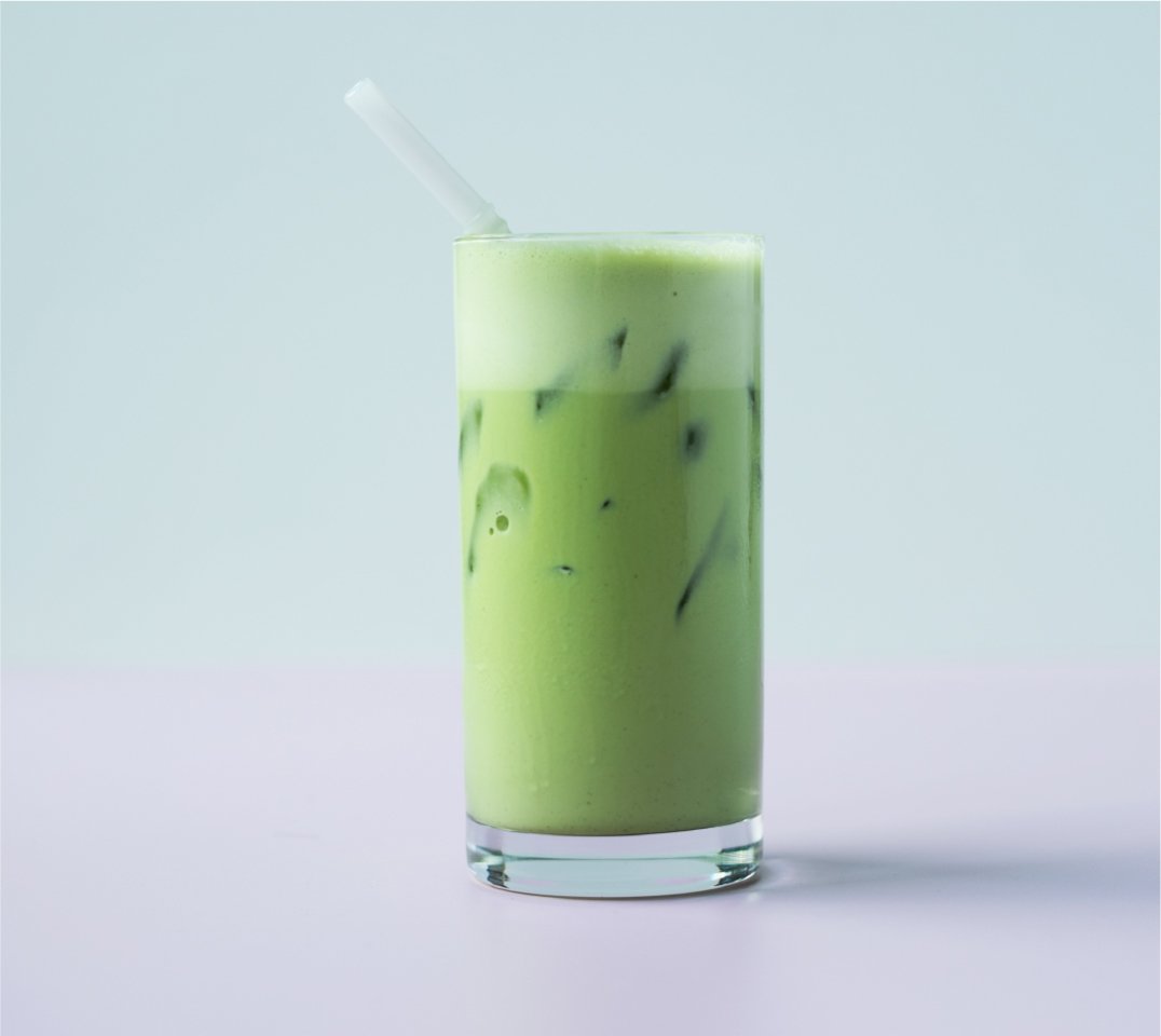 A tall glass of green juice with a straw standing on a purple surface