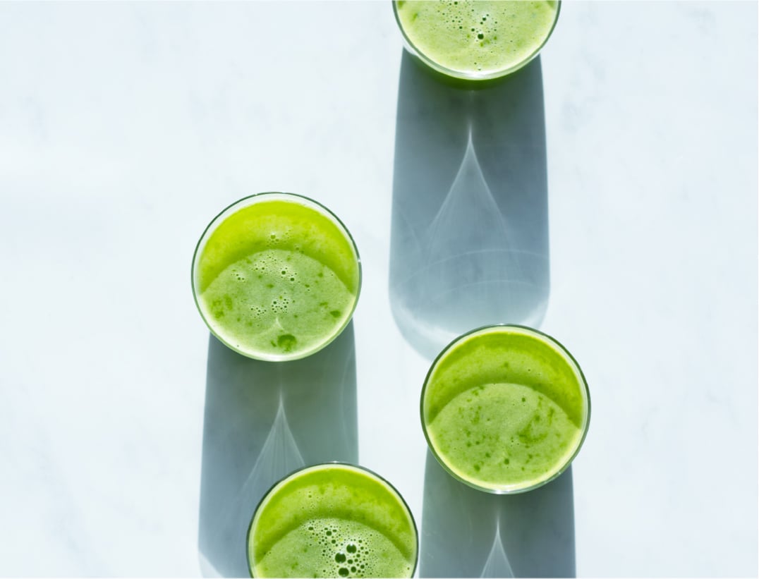 Overhead view of 4 glasses of spicy green garland juice on a marble counter 