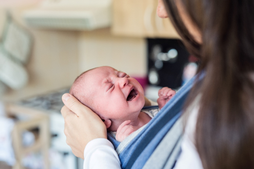 A newborn crying whilst held in a sling close to their mother.