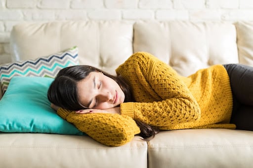 A woman is napping on the sofa. She is experiencing extreme tiredness in early pregnancy.
