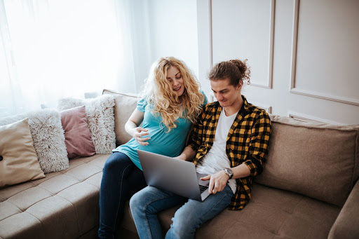 a pregnant couple are on the laptop researching how to register with a midwife.