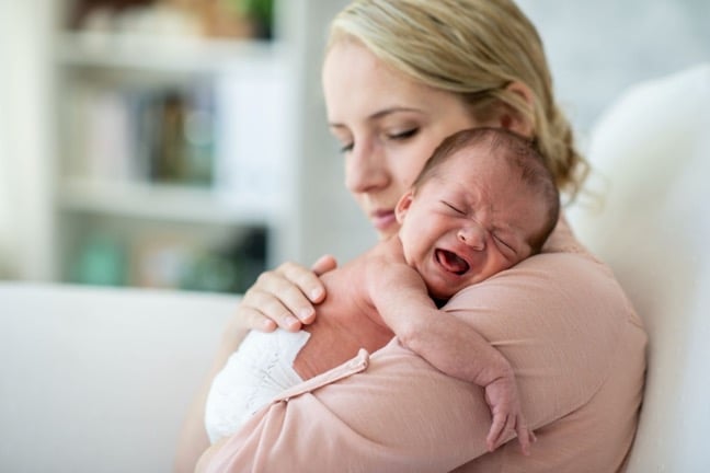 A baby crying in their mother's arms due to colic baby symptoms.