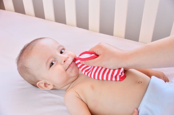 A baby is dribbling lots which is causing drool rash. The baby is lying in the cot, and their mother is wiping the excess dribble away from their face.