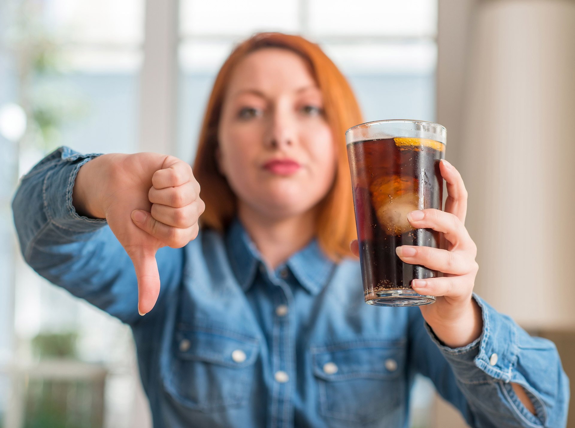 Woman holding soda refreshment with thumb down. Artificially sweet soft drinks are not foods that increase fertility in females