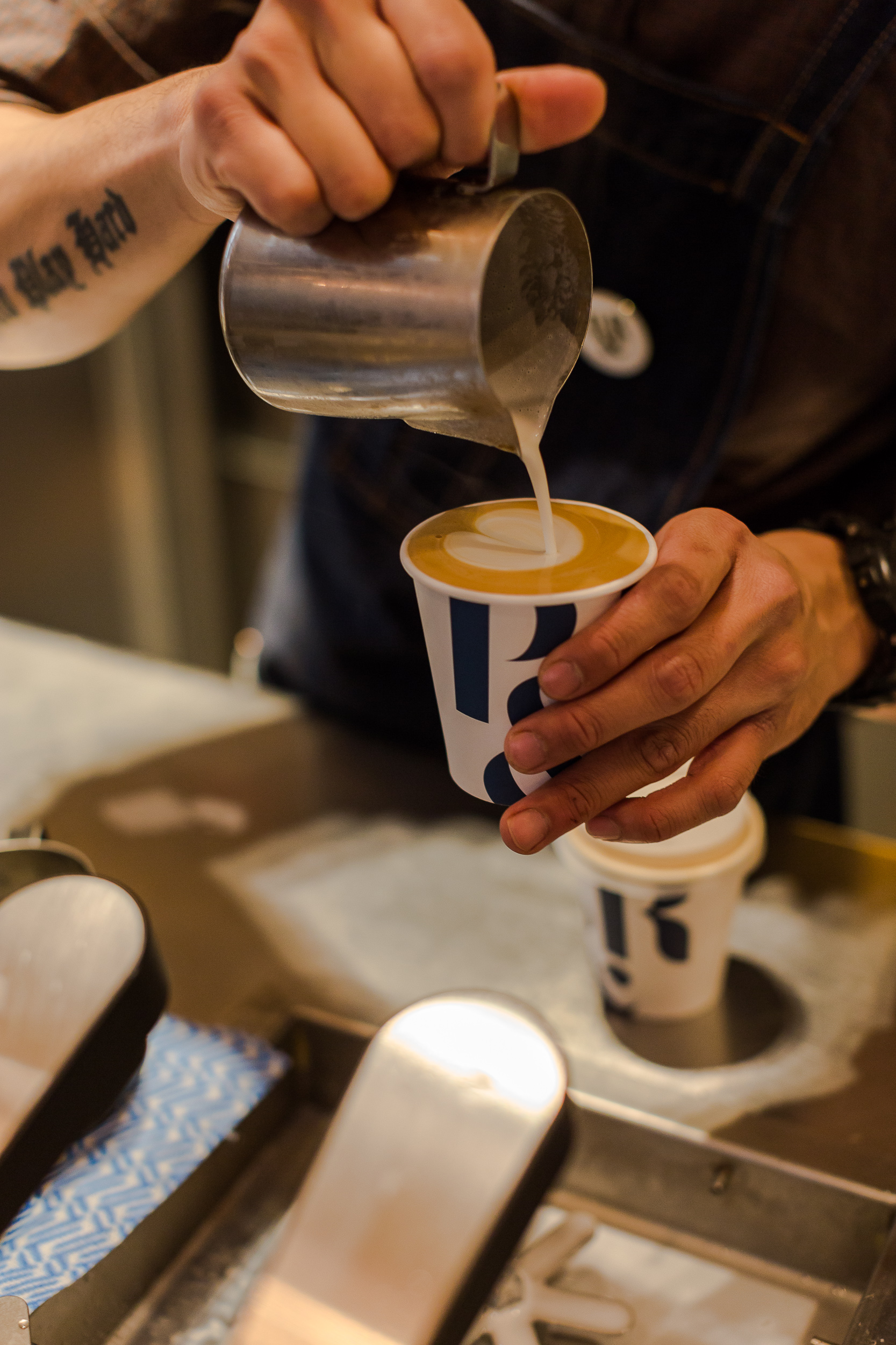barista pouring latte art into a P&R disposable cup