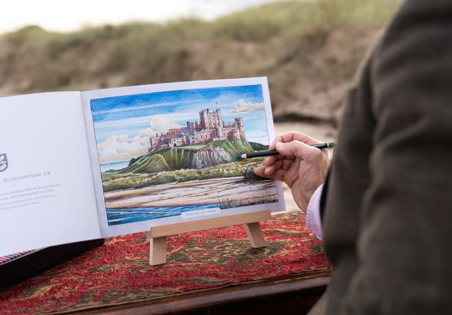 Un homme sur une plage en train de colorier le livre de coloriage de Castle Arts sur les magnifiques châteaux.