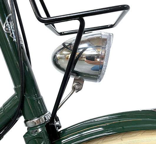 Side view of classic silver bike headlamp attached to top of bike forks on a green Pashley Princess.