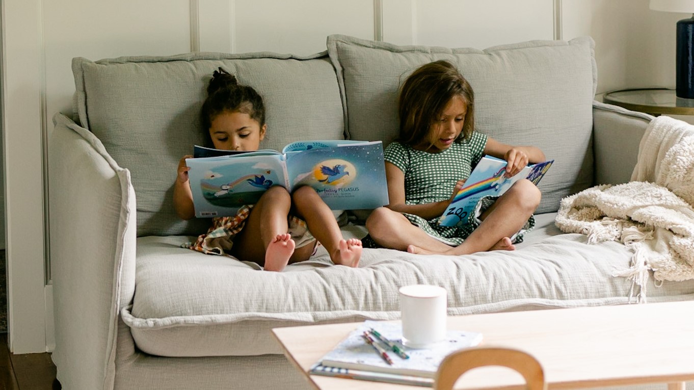 two kids reading books while sitting on the Neva Loveseat in Blanched Almond, Washed Cotton Linen