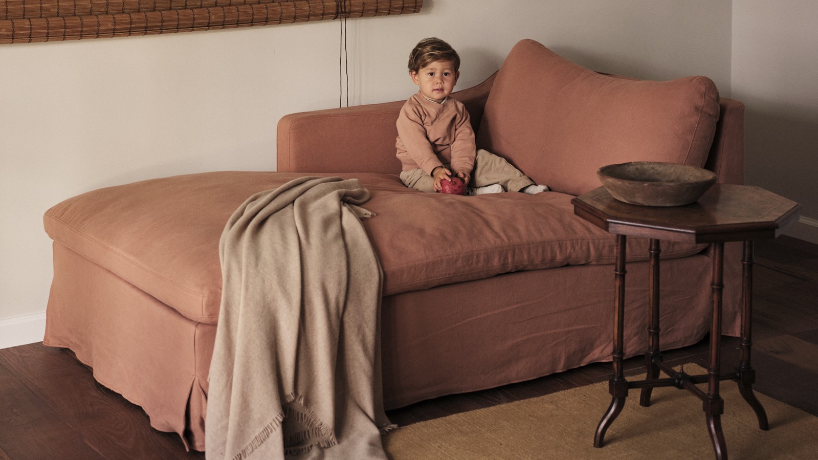 A baby sitting on the Amelia Left Arm Facing Daybed in Nectarine Dream, Thread-Dyed Cotton Linen