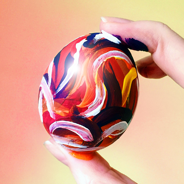 An egg painted with an abstract swirl pattern in acrylic paint.