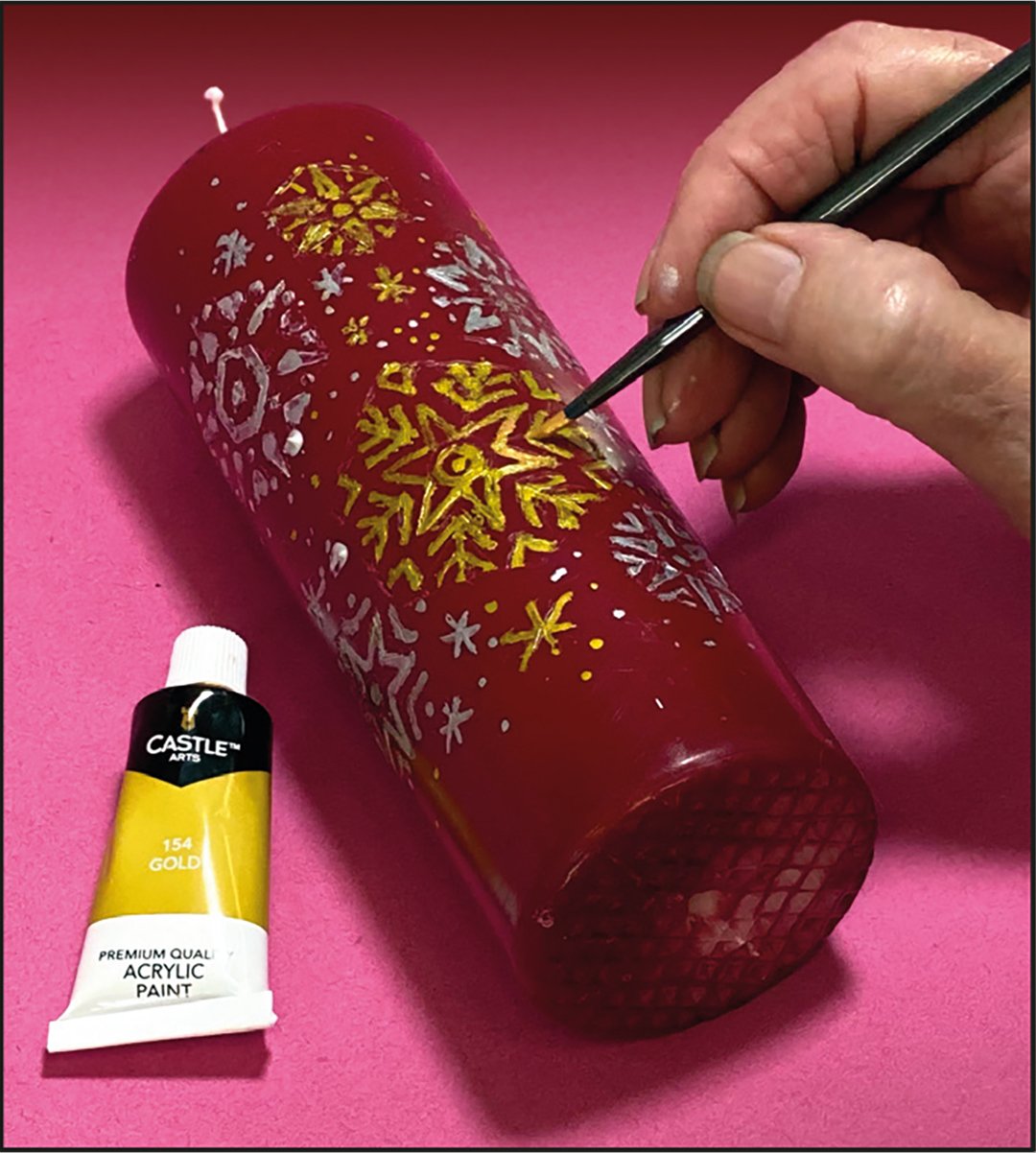 An artist adding gold acrylic paint to their Christmas candle.