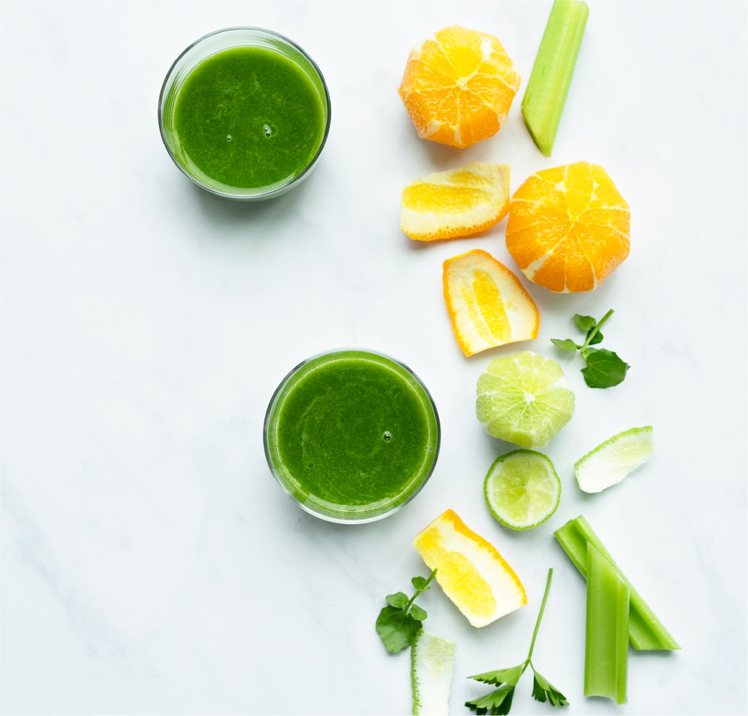 two glasses of green juice with ingredients on a marble surface