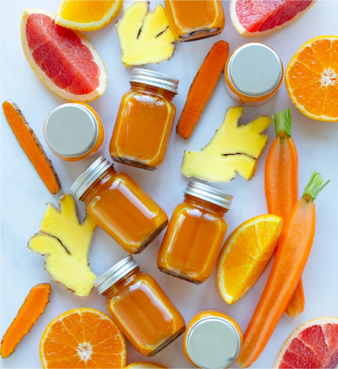 An array of small of bright orange recovery shot bottles with carrots and ginger
