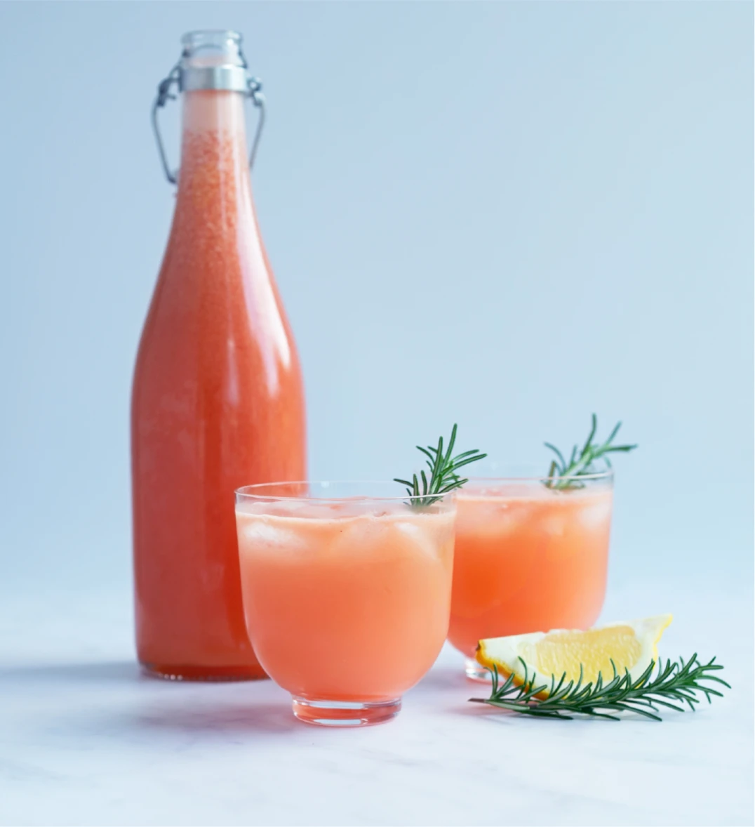 A tall bottle and two glasses filled with Ruby Red & Rosemary Spritz