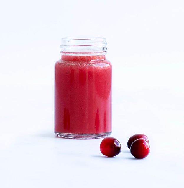 Small bottle of ginger wellness shot with 3 cranberries