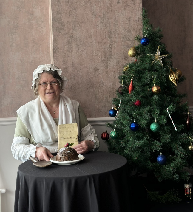 A person in a garment sitting at a table with a christmas treeDescription automatically generated