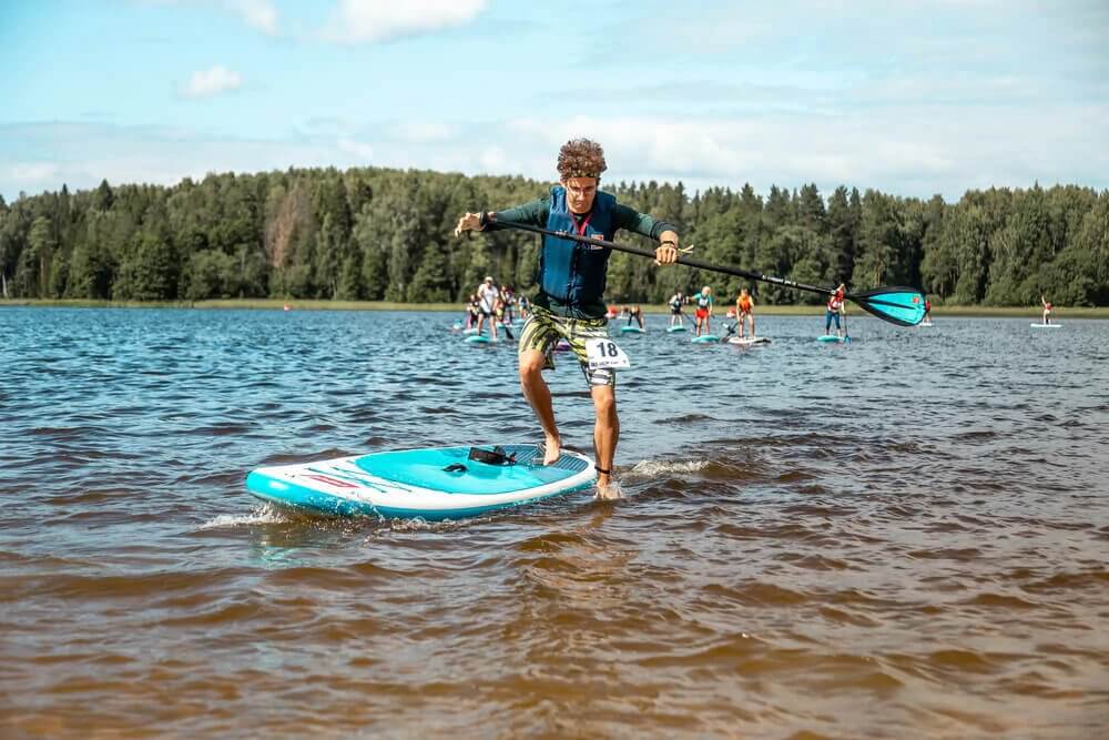 man stepping off a Red inflatable paddle board into the water whilst carrying a paddle