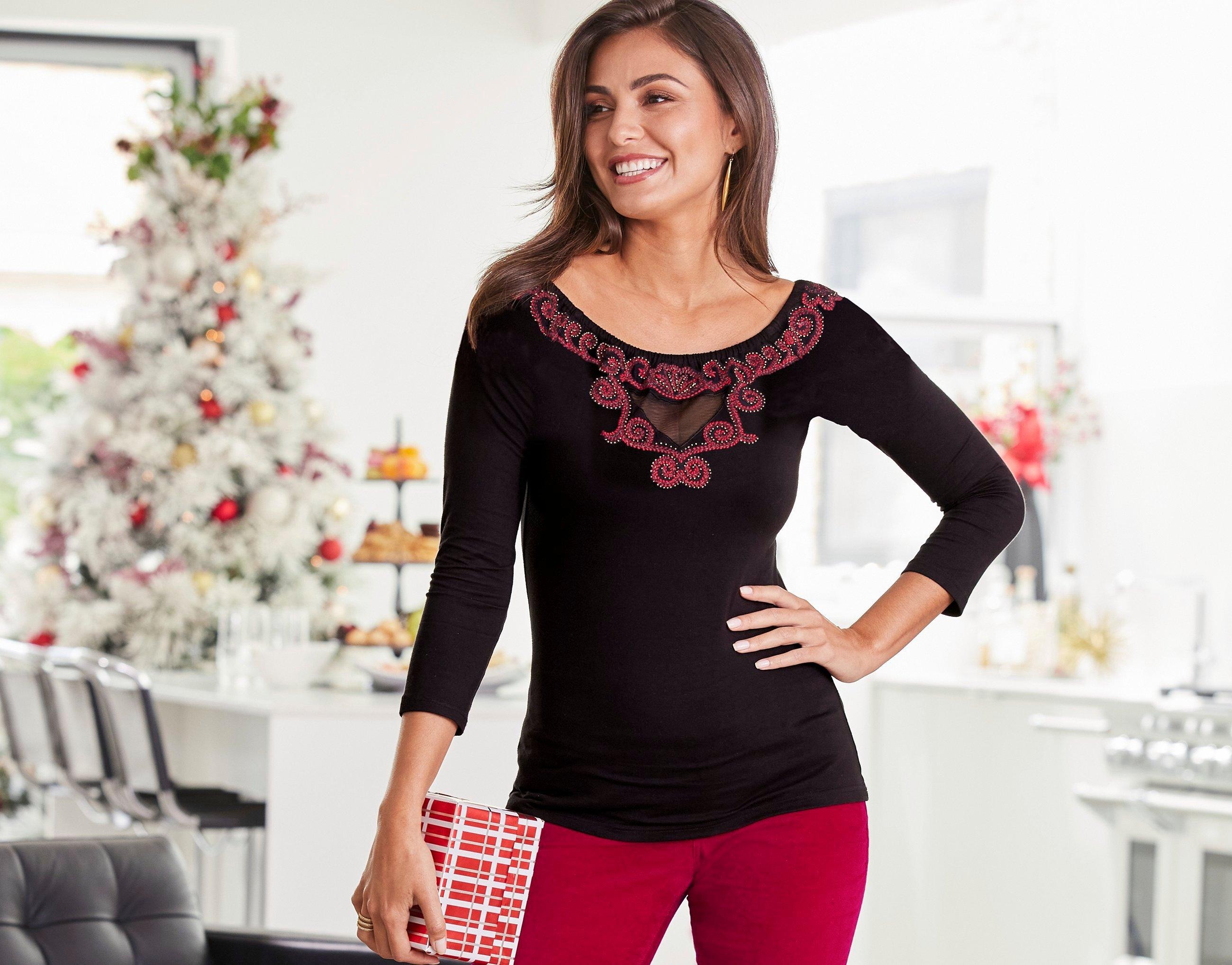 model wearing a black and red embroidered sweater and red velvet pants.