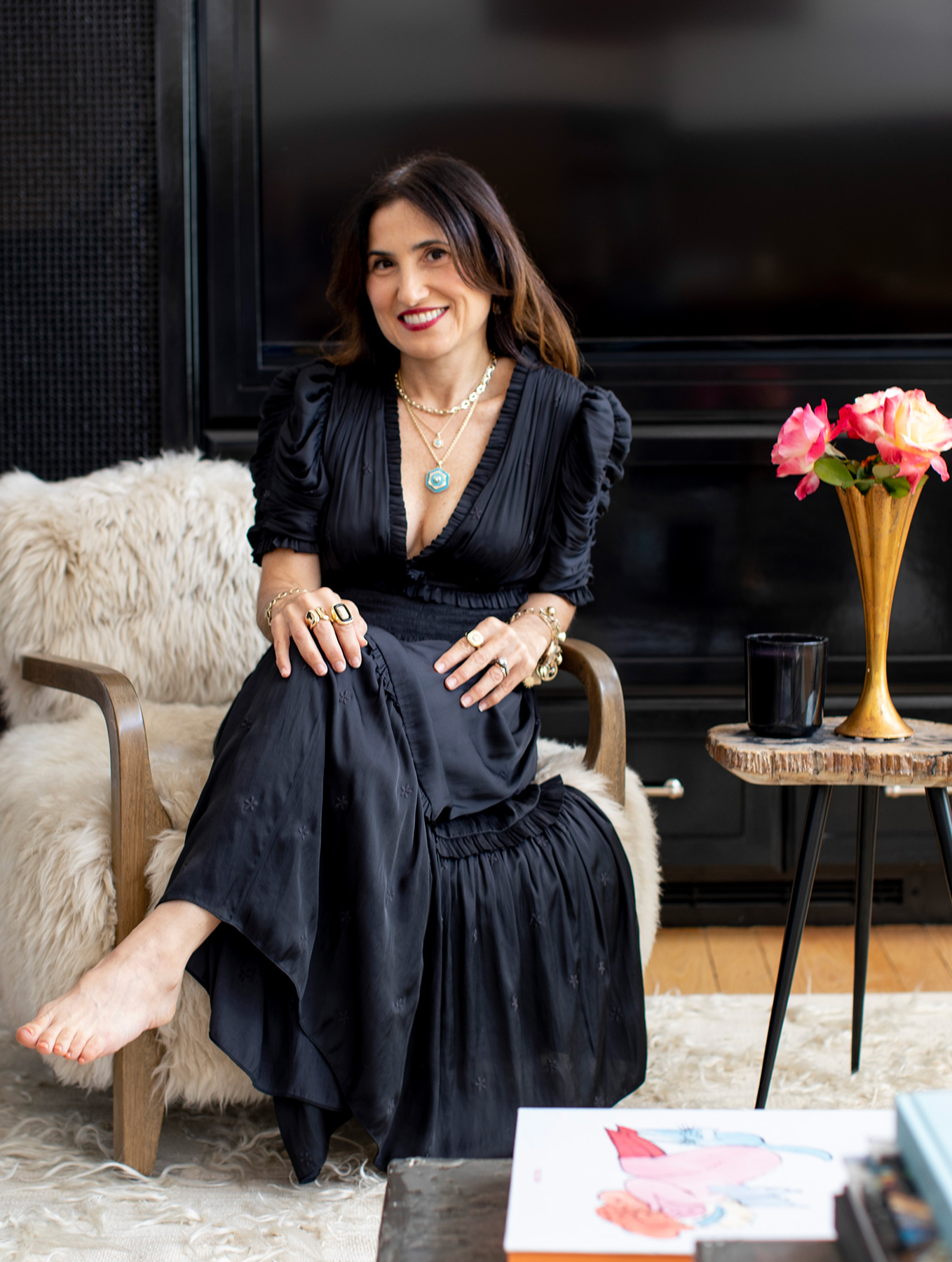 Gina Pell in front of bookcase wearing The Paloma Ring, Uncommon ring in Gold, The Double Apex Pendant, The Blade Pendant, The Fresh Cut Baguette Necklace, The Fresh Cut Oval Necklace, and The Fresh Cut Chandelier Drop Earrings