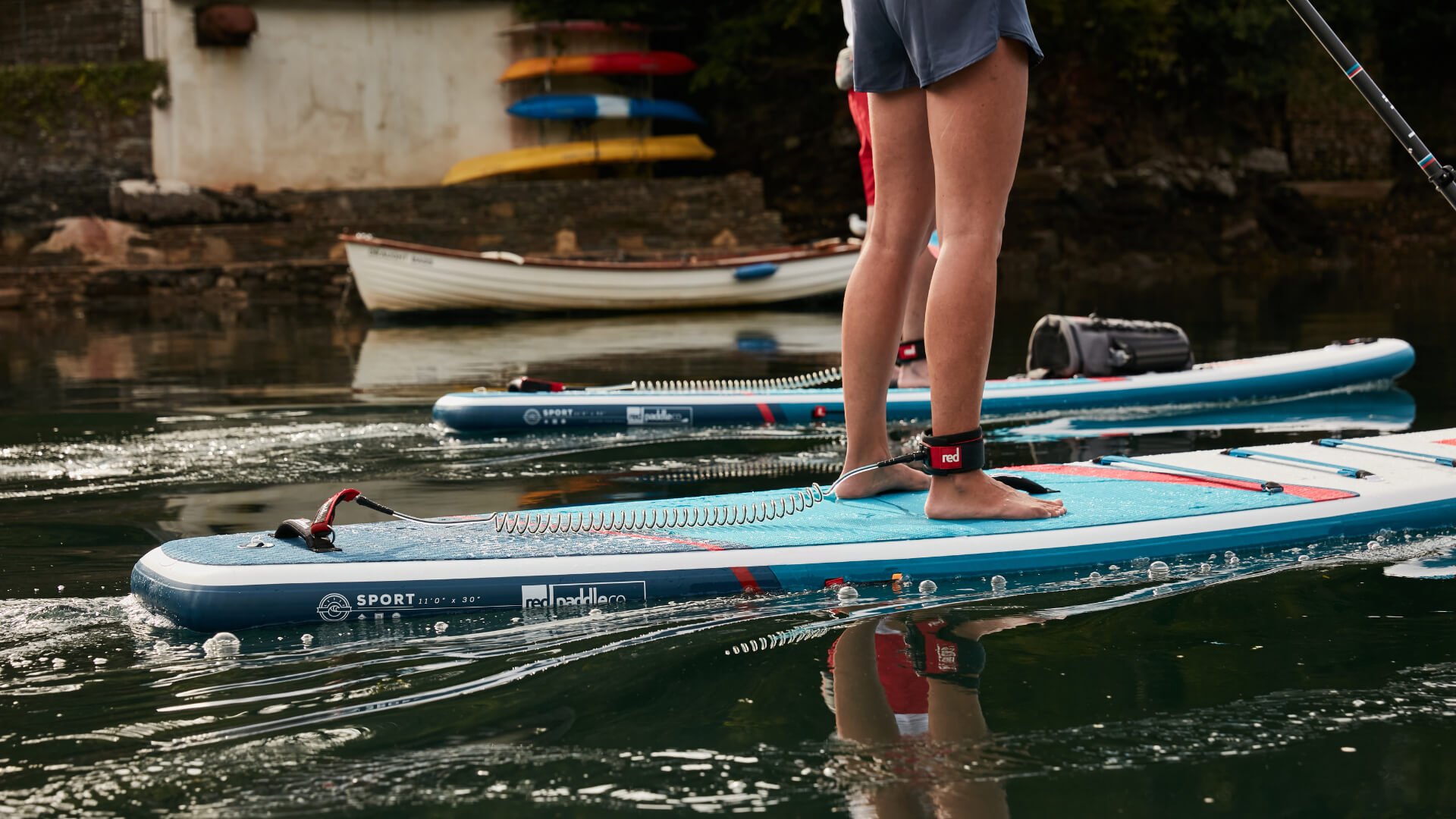 close up of woman paddling on Red stand up paddle board wearing a coiled SUP leash