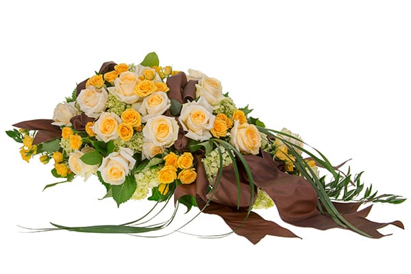 A gorgeous floral casket scarf mixes peach roses and spray roses, pale green hydrangea, lily grass, and Italian ruscus, then is finished with brown satin ribbons.