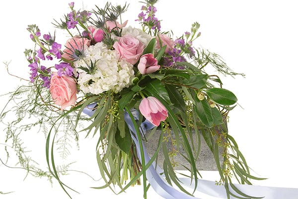 A beautiful Bespoke style hand tied bouquet mixes pink roses, white hydrangea, pink tulips, blue eryngium, purple freesia, seeded eucalyptus, and other foliages, and is tied off with a pale blue ribbon.