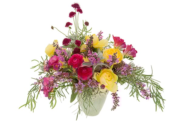 This beautiful Bespoke garden style centerpiece mixes fuchsia roses, yellow ranunculus, pink freesia, crimson scabiosa, hot pink pieris, and eucalyptus in a teal ceramic vessel.