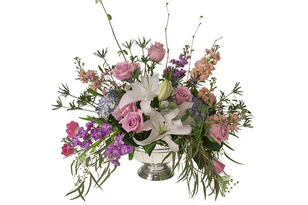 This Bespoke style centerpiece features pink roses, white lilies, lavender snapdragons, blue hydrangea, eryngium, eucalyptus, and other foliages in a silver compote.
