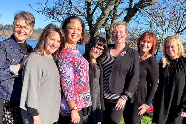 This lovely group photo of seven Floral Design Institute Instructors is taken outdoors under spring trees.