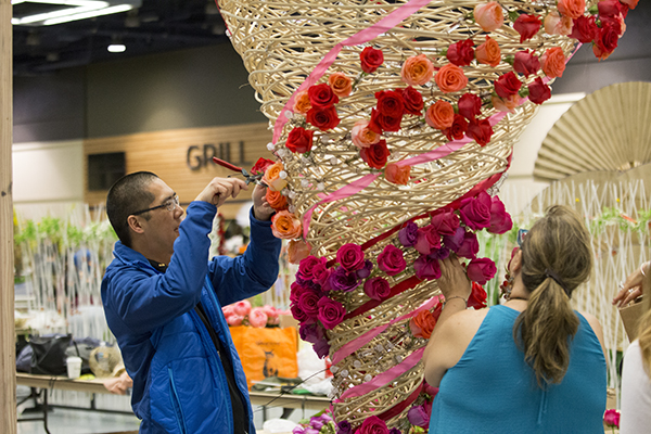 A large floral installation made of cane is covered in spirals using vibrant red, coral, and peach roses and ribbons.