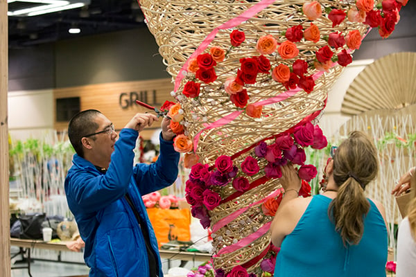 A large floral installation made of cane is covered in spirals using vibrant red, coral, and peach roses and ribbons.