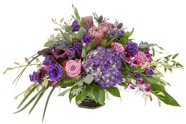 This elegant wedding centerpiece combines purple hydrangea, variegated pink roses, champagne protea, orchid blossoms, eryngium, seeded eucalyptus, lily grass, fatsia leaves, and Italian ruscus.