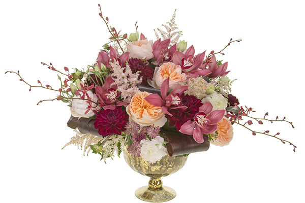 This lavish wedding centerpiece mixes cranberry orchids, peach garden roses, burgundy dahlias, astrantia, astilbe, and rolled ti leaves in a gold compote.