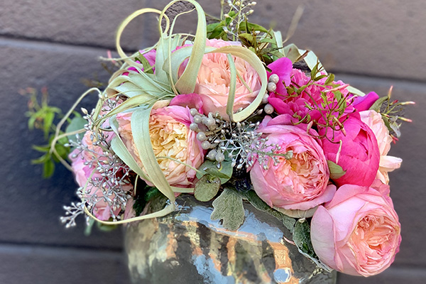 A beautiful floral design in pink hues is created from garden roses, peonies, seeded eucalyptus, and other foliage. 