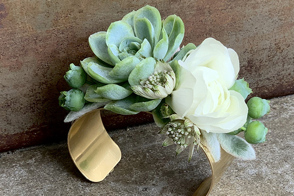 A lovely wrist corsage is created using succulents and an ivory bloom on a gold cuff.