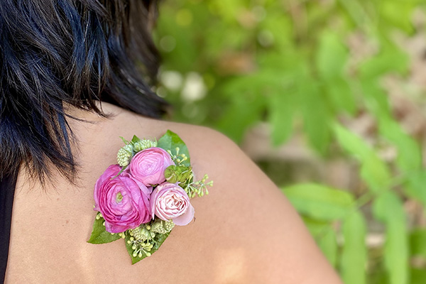 A delicate shoulder corsage in pink hues is composed of ranunculus and bits of seeded eucalyptus.