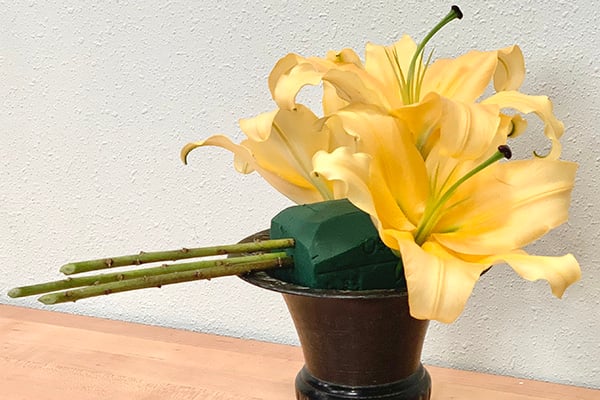 Add lilies on one side of the foam, then insert cut lily stems horizontally on the other side for balance and contrast.