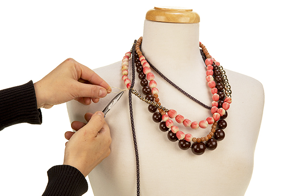 The addition of more necklace strings, some with real beads to create an interwoven bundle of necklaces.