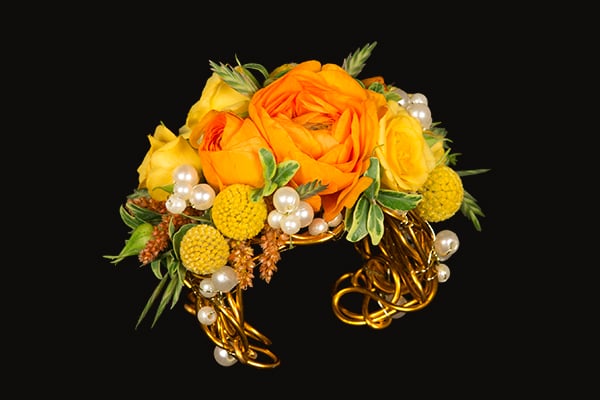 A gorgeous, over-the-top homecoming cuff with lots of bling is covered in orange roses, bright yellow spray roses, and sunshine colored craspedia for a beautiful style.