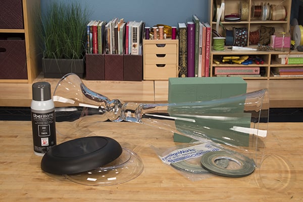 Materials for this design include a tall clear glass trumpet vase, waterproof tape, floral foam Lomey dishes, hydrangeas, roses, plumosa and ruscus.