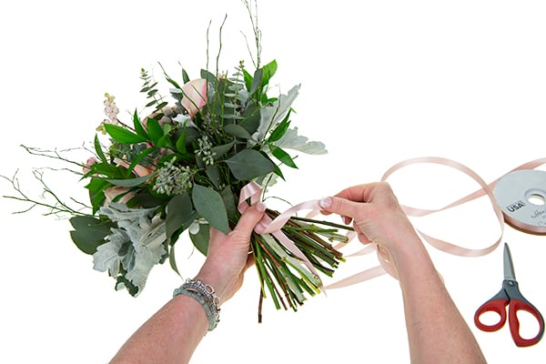 a hand-tied bouquet showing the start of wrapping the stems with ribbon