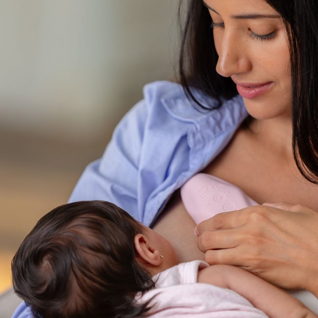 Mother breastfeeding baby, using Dr. Talbot's Lactation Massager.