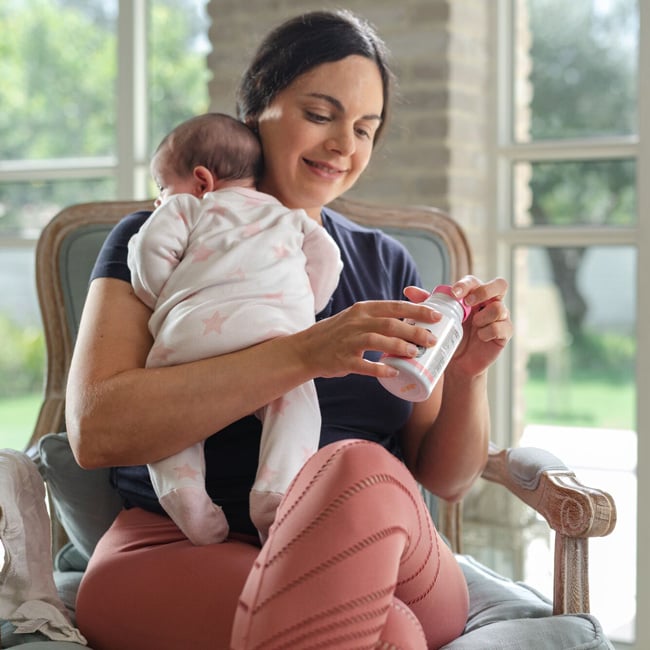 Mother holding baby while taking Dr. Talbot's Lactation Support Vitamins.