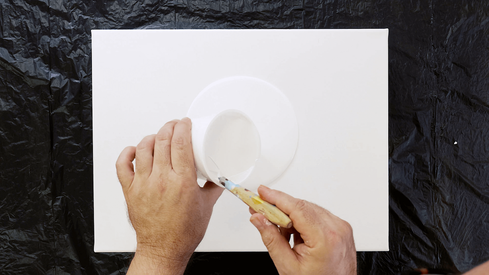 Hand pours white acrylic pour paint onto a white canvas.