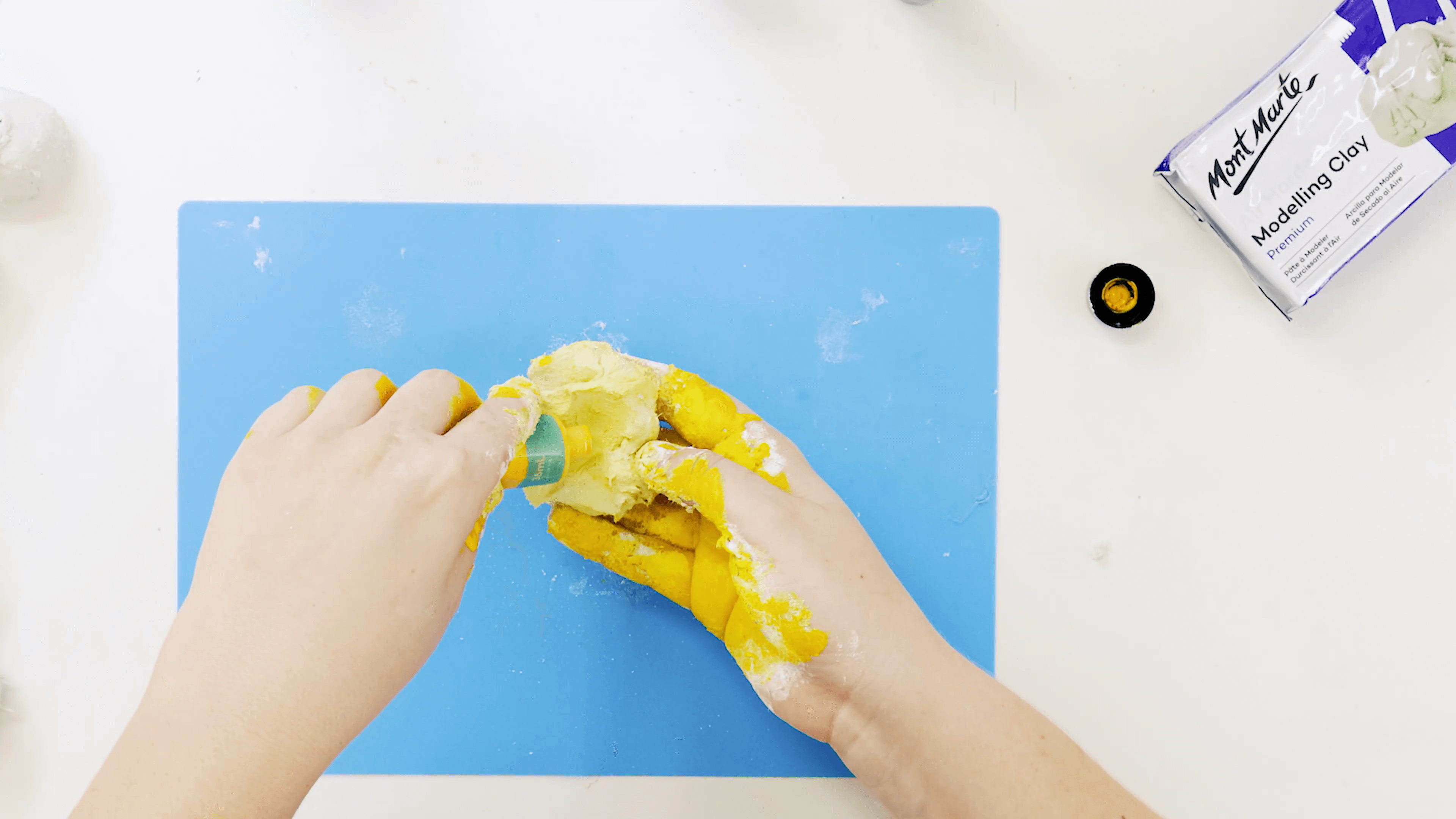 A hand squeezing yellow acrylic colour paint into the air dry clay ball.