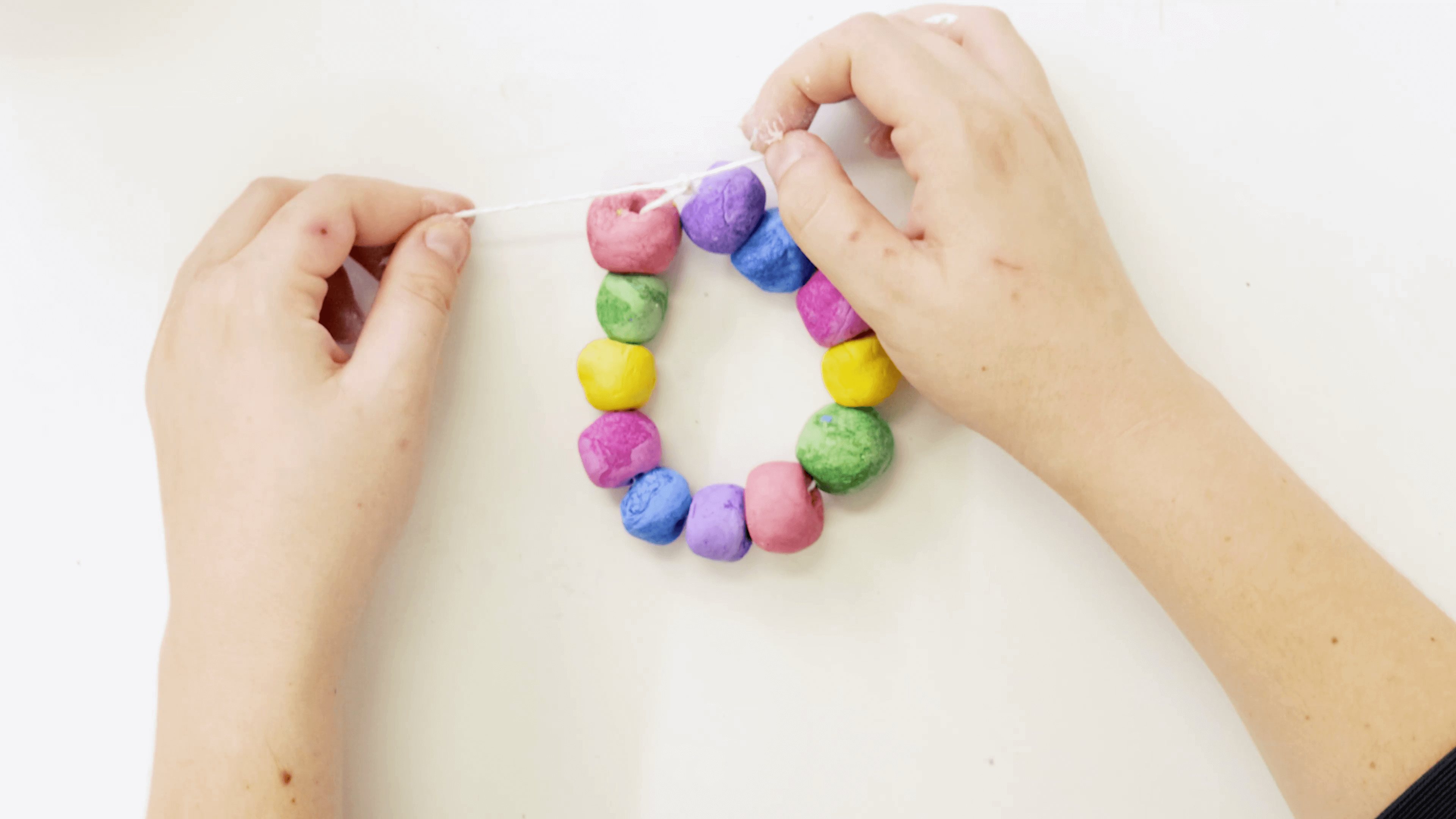 Hand tightening the string of a brightly coloured air dry clay bracelet